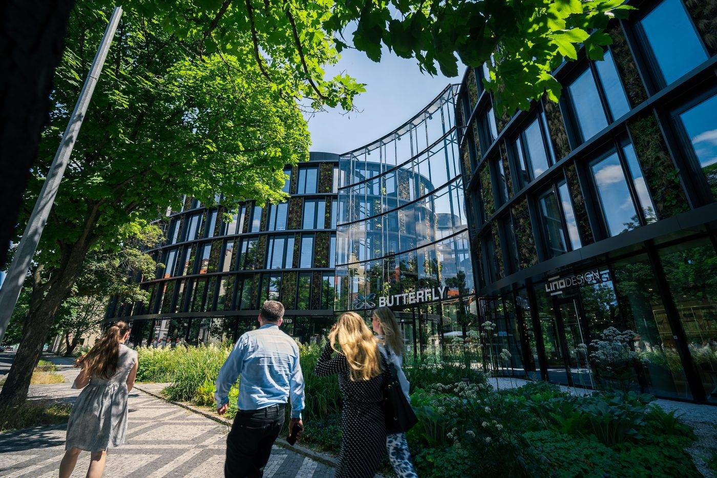 Moderní kancelářská budova se zelení a lidmi u vchodu