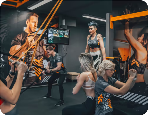 Skupinové cvičenie s odporovými gumami v tmavom fitness centre s oranžovými prvkami